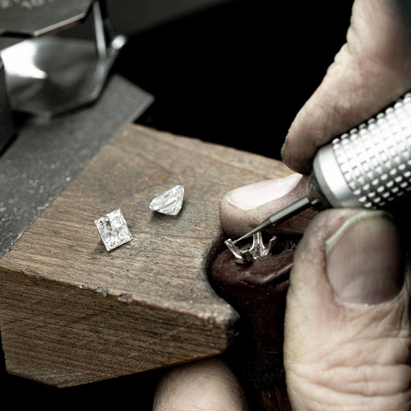 Jeweller sitting at bench setting diamond into ring