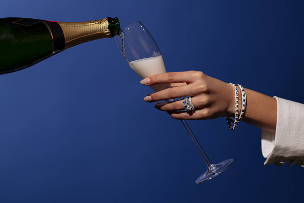 Model wearing diamond and sapphire jewellery holding a glass of champagne