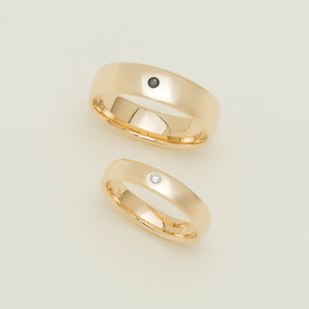 Two yellow gold Milestone Bands on neutral background. One set with a single sapphire and one set with a single white diamond.