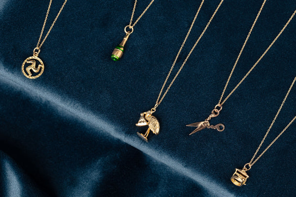 Various gold charms on gold chains including champagne bottle, stork with baby and scissors