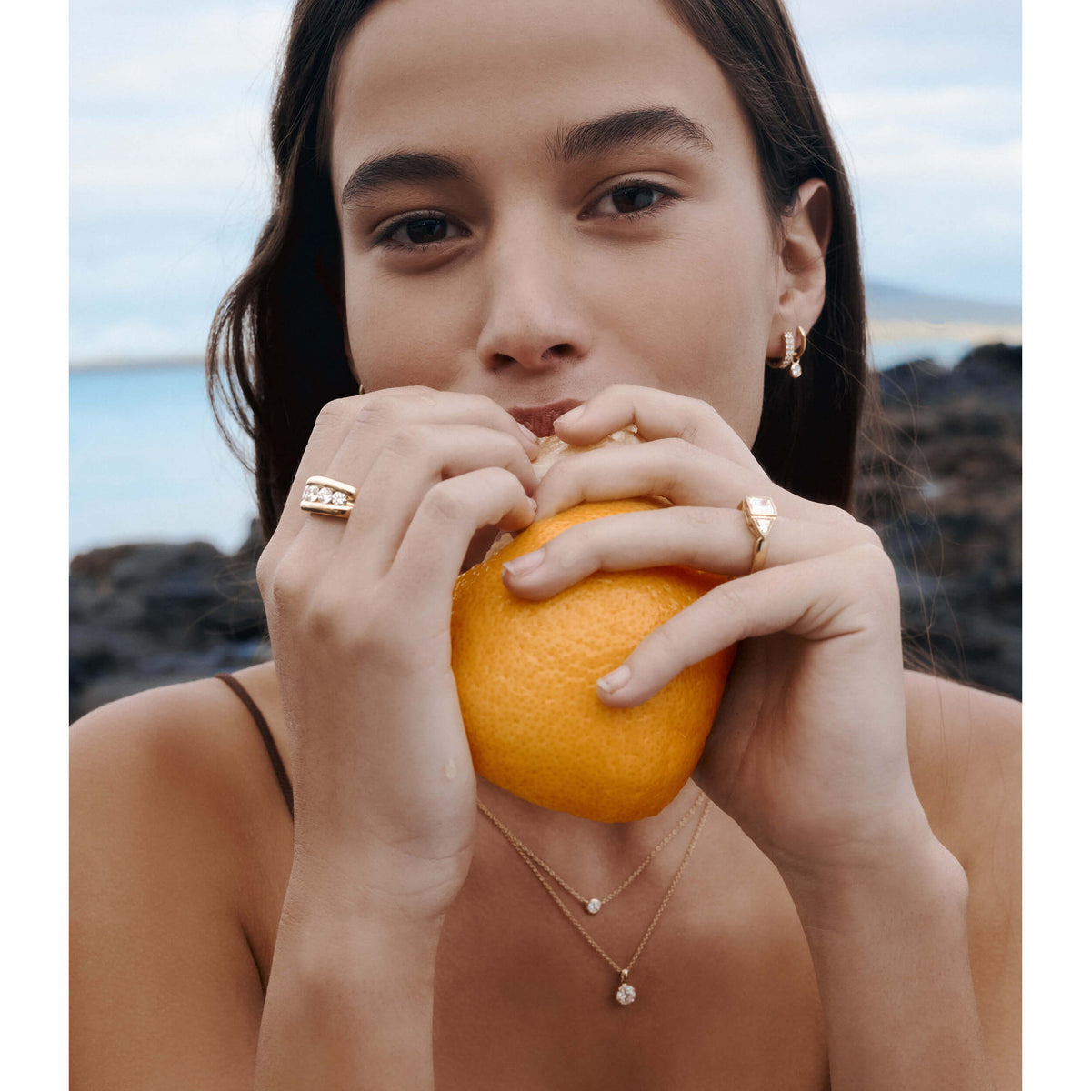 Model wearing natural diamond rings, earrings and necklaces and eating an orange