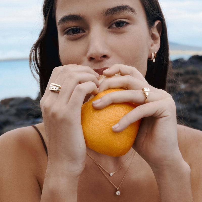 Model wearing diamond jewellery biting into an orange on NZ beach