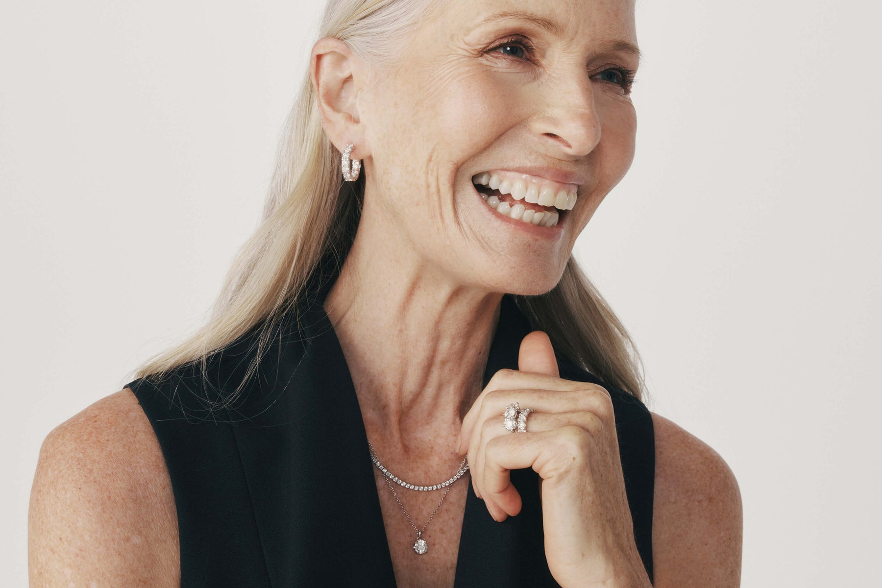 Woman smiling wearing diamond hoop earrings, diamond wedding and engagement rings and diamond necklaces