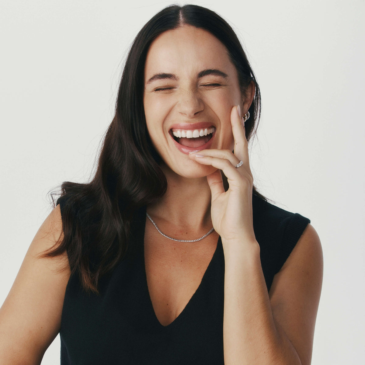 Woman smiling wearing diamond necklace, rings and earrings against a neutral background
