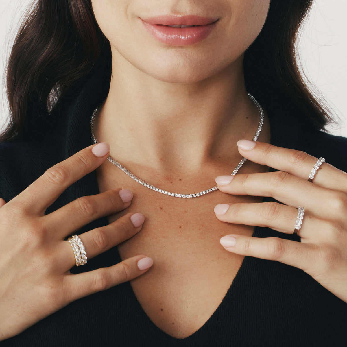 Woman wearing a diamond necklace and rings on a plain background