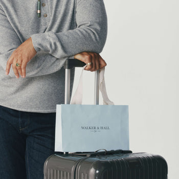 Man holding the handle of a suitase with Walker & Hall gift bag resting on top.