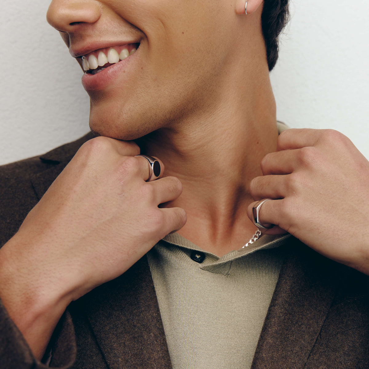 Man smiling wearing two silver signet rings and a silver chain