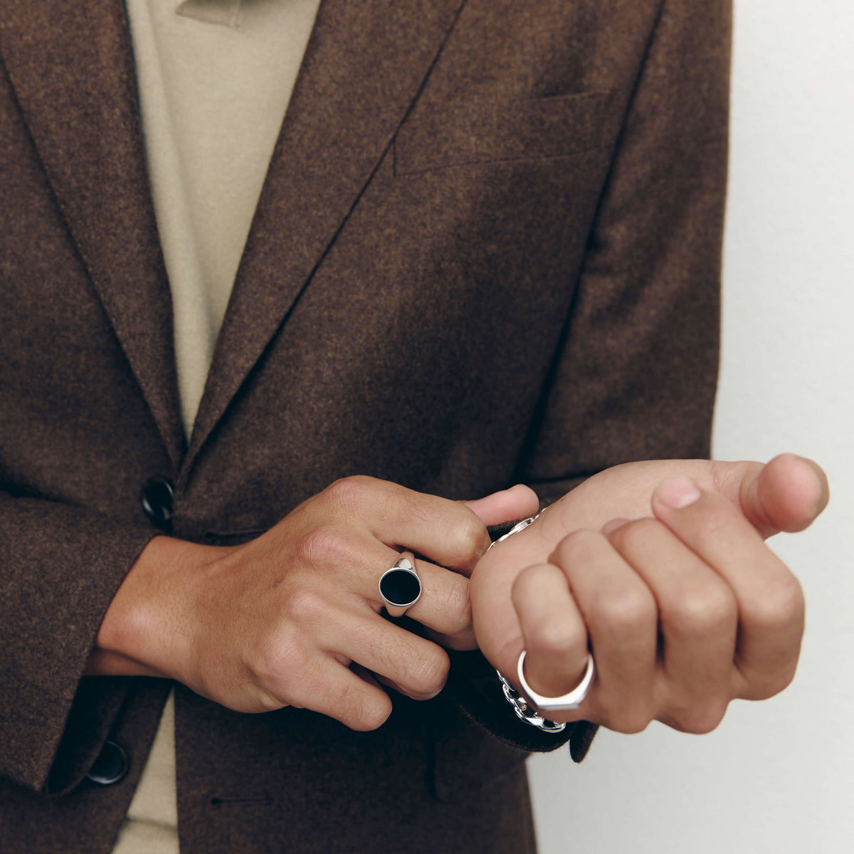 Close up of a man's hands wearing silver signet rings while he adjusts a silver chain bracelet