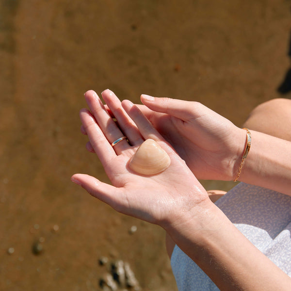 Model holding a shell on NZ beach, wearing gold ring and bracelet