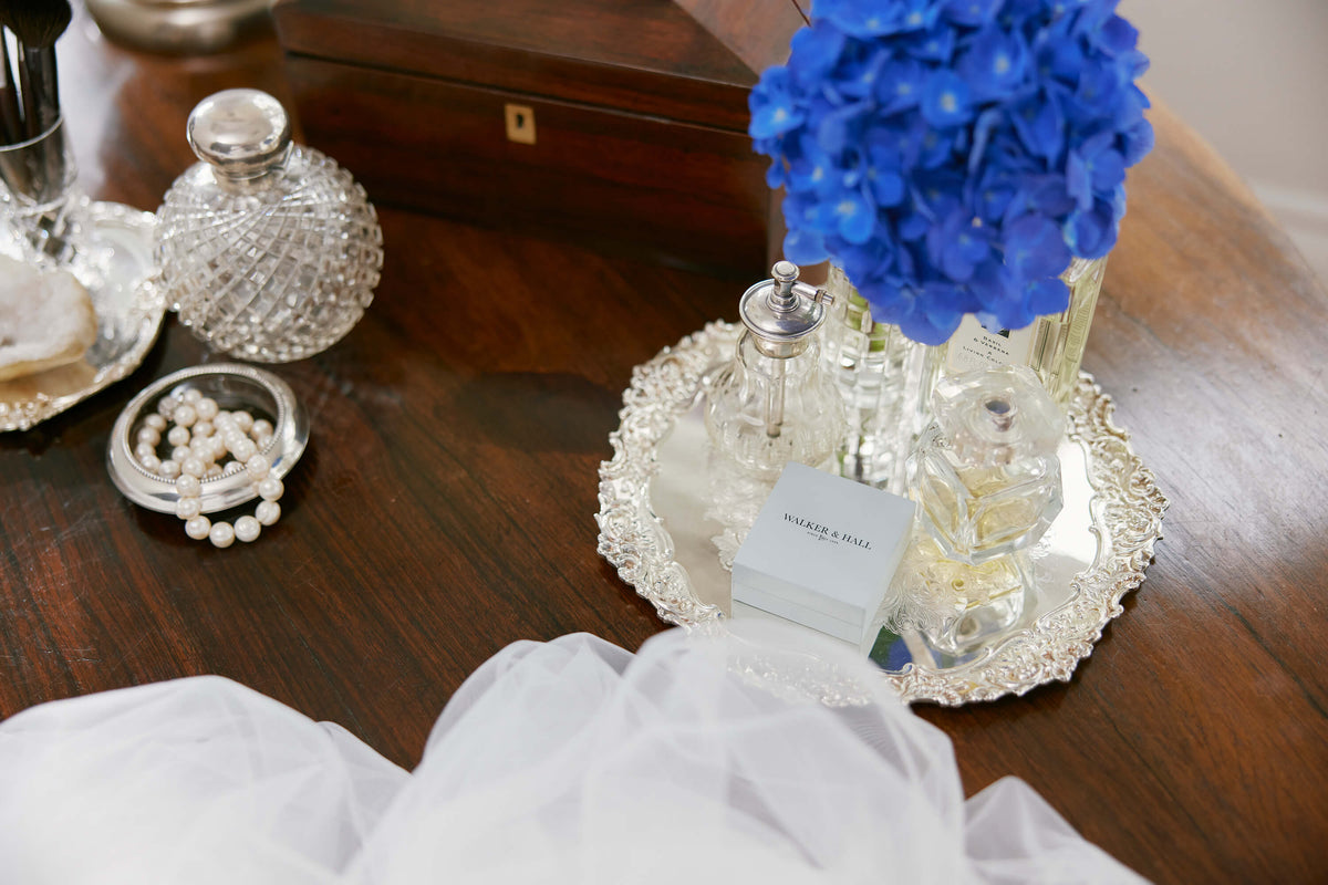 Pearl strand and Walker & Hall jewellery box on set of wooden drawers with perfume bottles and vase of flowers